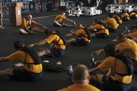 Sailors do post-workout stretches in the hangar bay of the aircraft carrier USS Nimitz.
