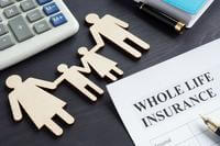 An assortment of desk items, a form labeled &quot;whole life insurance&quot; and wood cutouts representing a family appear on a desk